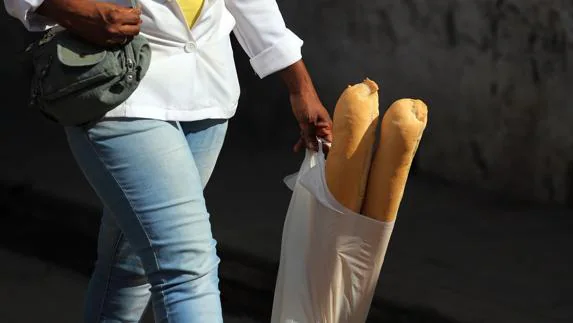 Una mujer lleva dos barras de pan en una bolsa de plástico.