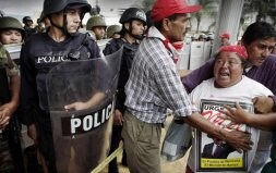 Dos hombres intentan apartar de la barrera policial a una seguidora de Zelaya, que muestra un póster en apoyo del presidente derrocado. / AP