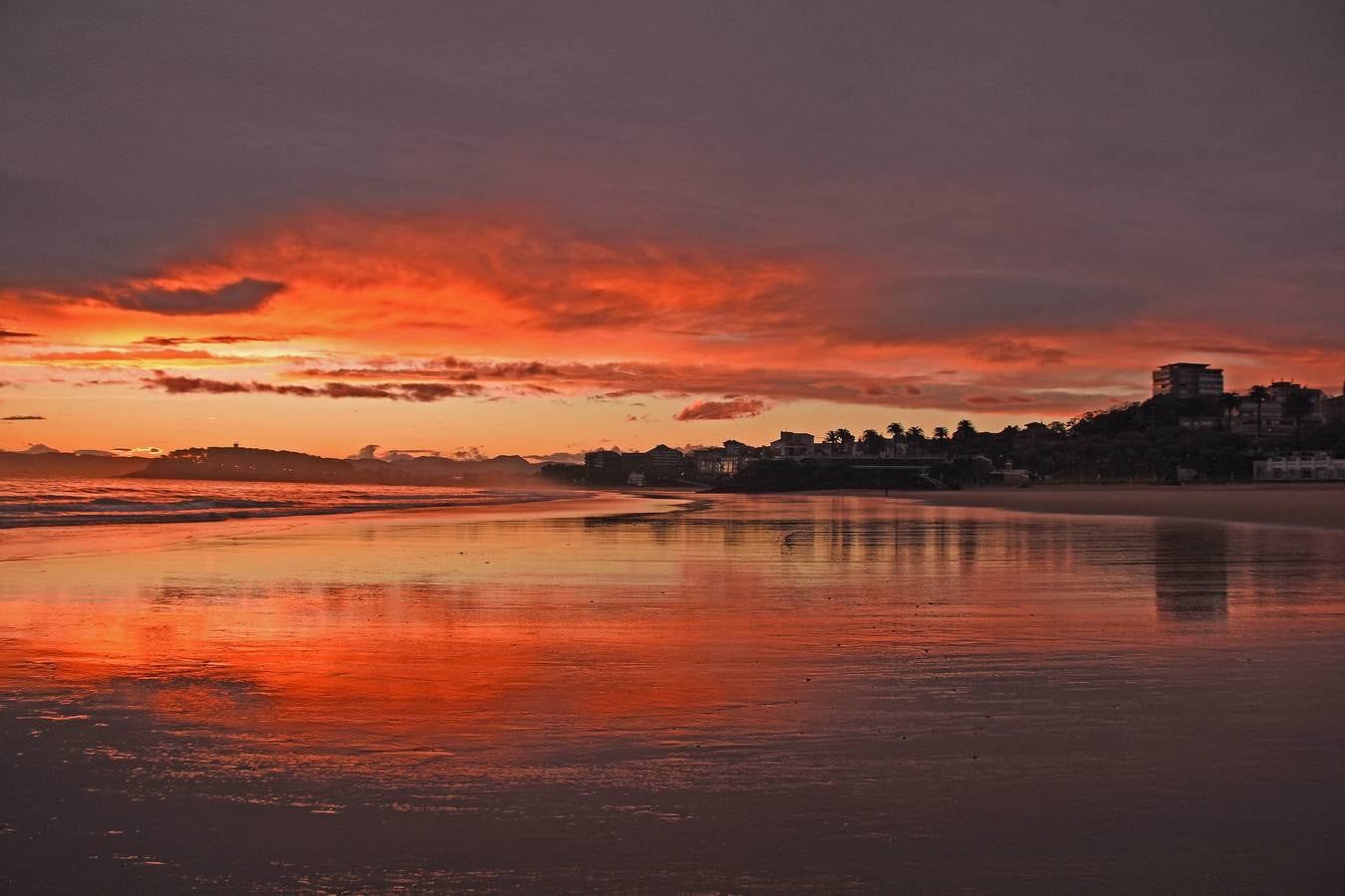 Un cielo naranja se refleja en la arena mojada de la segunda playa de El Sardinero,