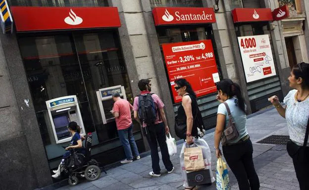 Gente haciendo cola en los cajeros de una sucursal del Banco Santander en Madrid.