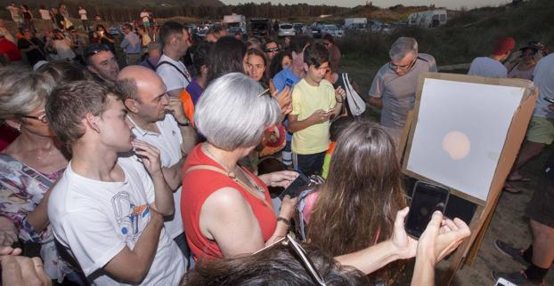 Múltiples curiosos observan el sol gracias a un filtro poco antes del eclipse parcial desde el observatorio que se montó en la playa de Liencres.