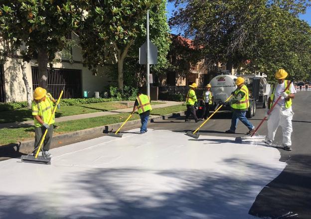 Un grupo de operarios extiende el revestimiento especial de color blanco, Coolseal, sobre el asfalto de una calle de Los Ángeles. 