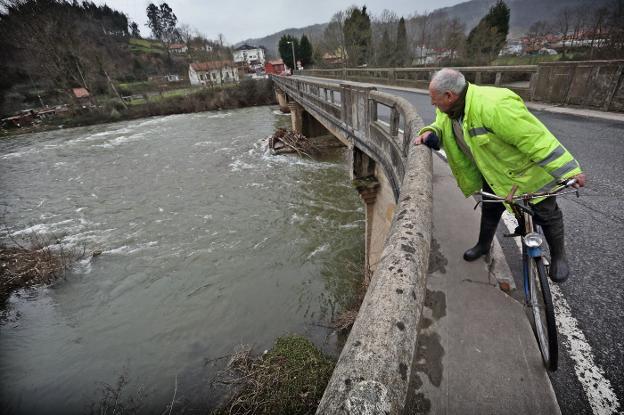 Un vecino observa el río Saja desde el puente que separa Virgen de la Peña y Villanueva de la Peña.