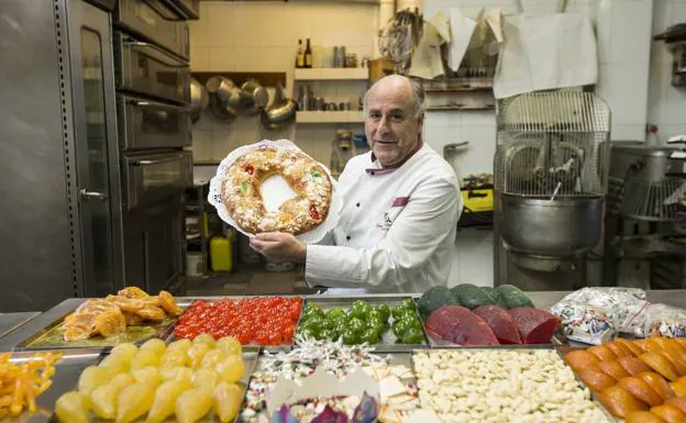 Luis Salas sostiene un roscón junto a una mesa de su obrador llena de ingredientes y de detalles vinculados a la tradición.
