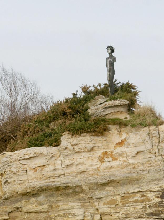 Arriba, imagen de la escultura Neptuno Niño, en el promontorio de la playa de El Camello poco antes de ser retirada.