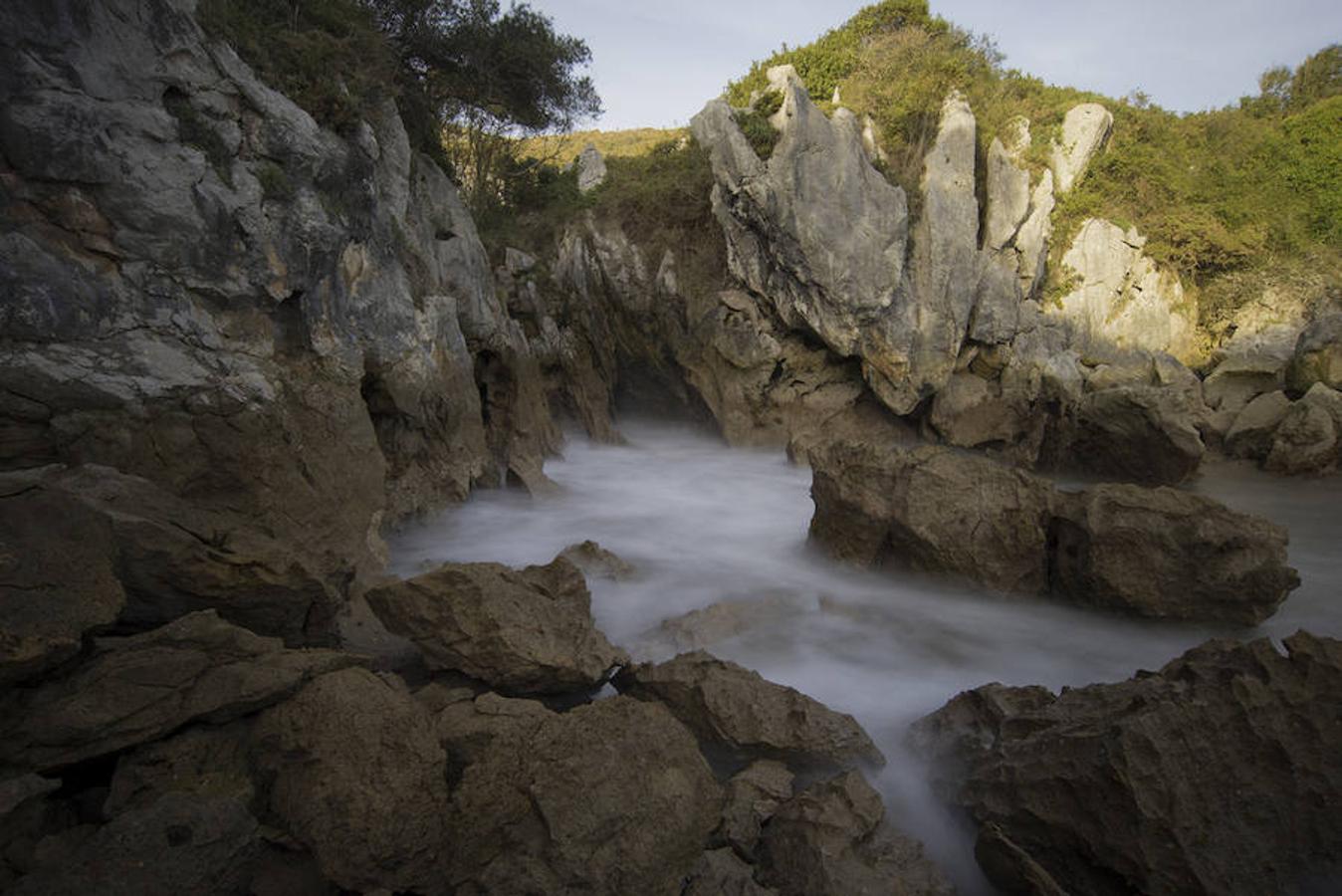 Playa de Gulpiyuri (Asturias) | Bastante aislada e intacta, esta curiosa ‘playa’ se encuentra tierra adentro y entre prados, apresada en una costa de acantilados cavados por el mar y un hundimiento que provocó un hueco justo a 100 metros del mar, pero conectado con su corriente. El resultado es este rincón escondido y paradisíaco.