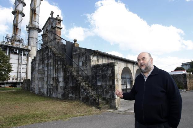 El párroco muestra el exterior de la iglesia, rodeada por las instalaciones de la fábrica de Sniace.