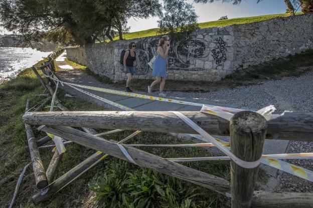 Dos visitantes pasan frente a los desperfectos de las vallas de la senda de Mataleñas, en Cabo Menor. 