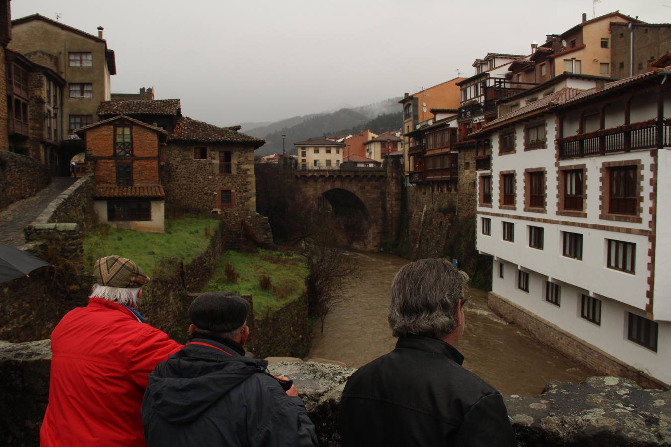 Varios vecinos contemplan la crecida del río Quiviesa a su paso por Potes desde el puente de San Cayetano