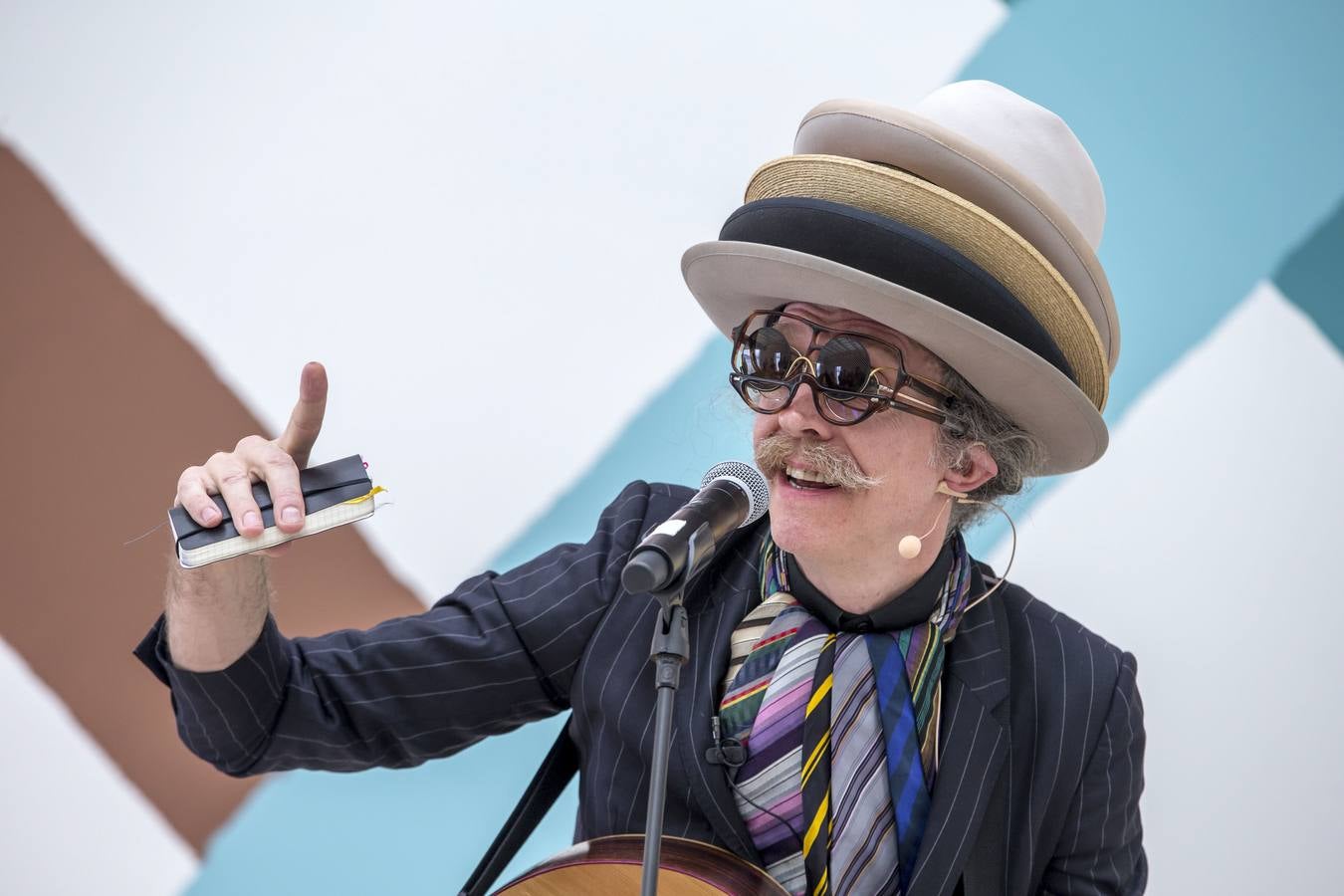El artista, vestido de manera acorde con los músicos y con tres gafas de sol y cuatro sombreros superpuestos.