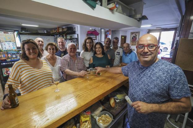 Quique Pazos y sus clientes sonriendo en la barra del bar. 