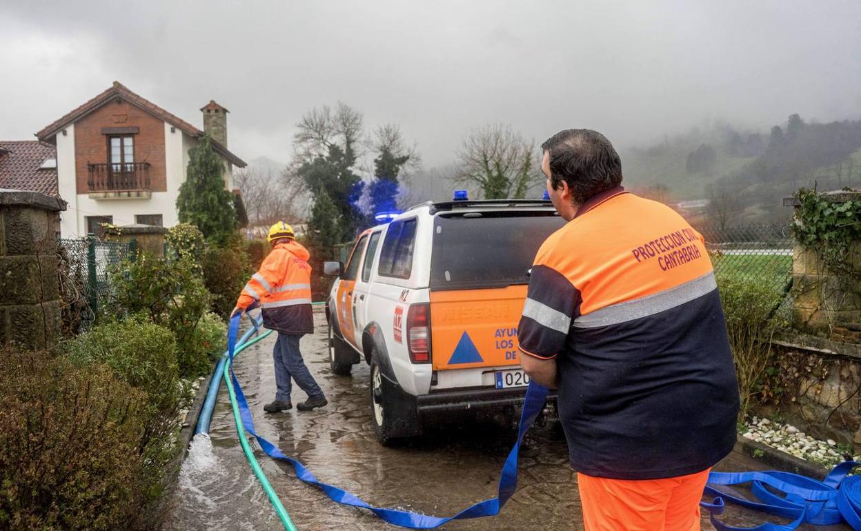 Un vecino es ayudado por miembros de Protección civil a achicar el garaje de su vivienda en Los Corrales de Buelna