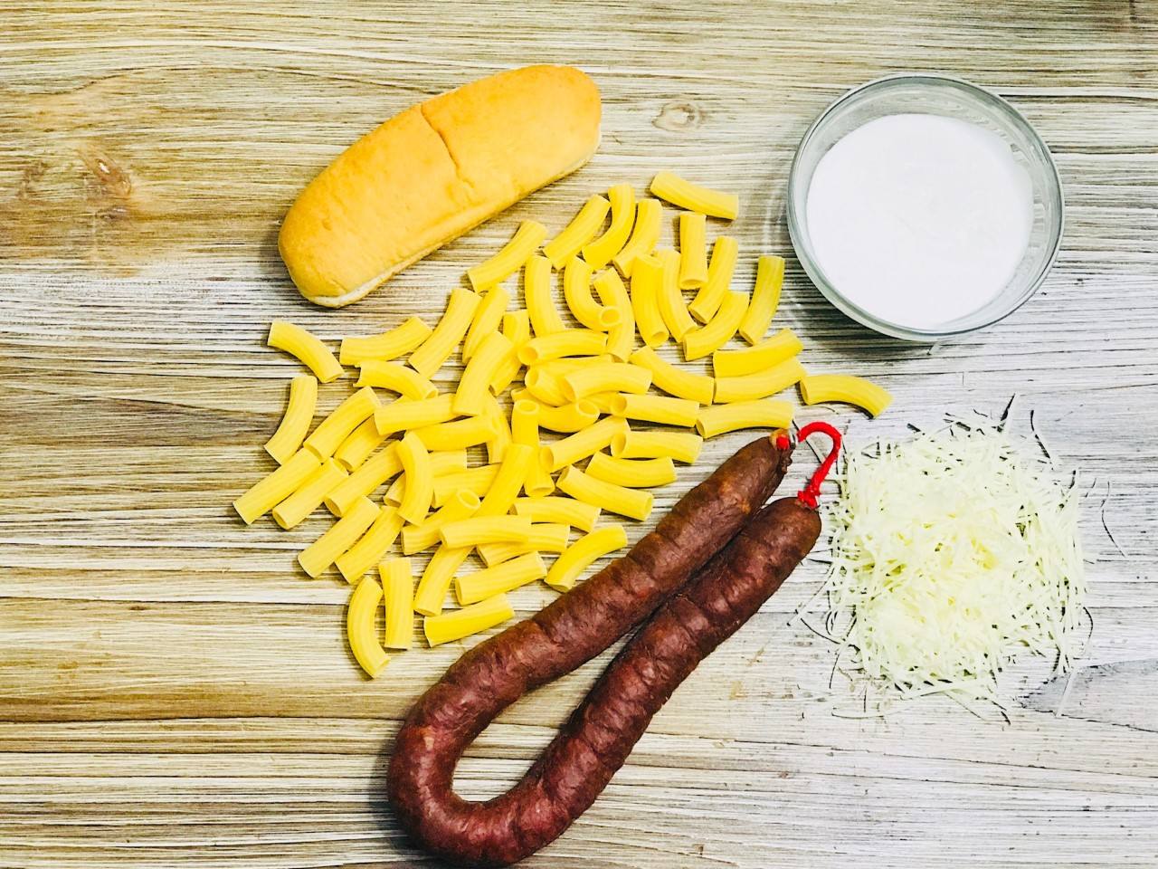 RIGATONI CON CHORIZO DE POTES. Ingredientes: 6 panes de 'hot dog', rigatoni 250 gramos, nata para cocinar 750 mililitros, chorizo de Potes (cantidad al gusto de cada uno), queso rallado para gratinar 200 gramos, pimienta negra, sal y aceite de oliva virgen extra. Opcional: Hierbas provenzanas.