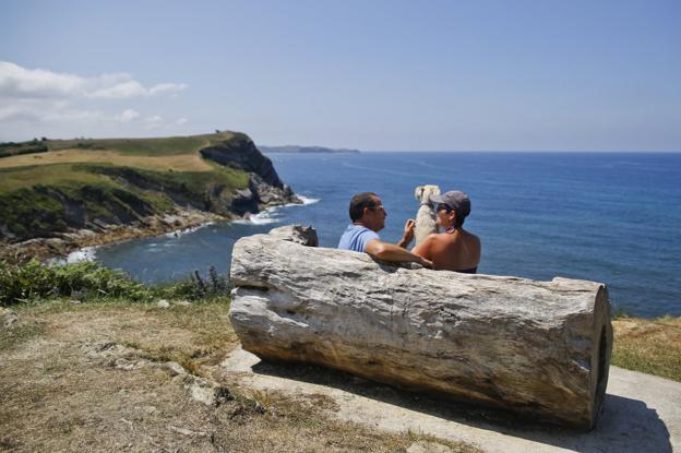 Andy y Denis acarician a su perro 'Gordi' sentados en el banco que hay en el mirador de La Corneja, en Liandres.