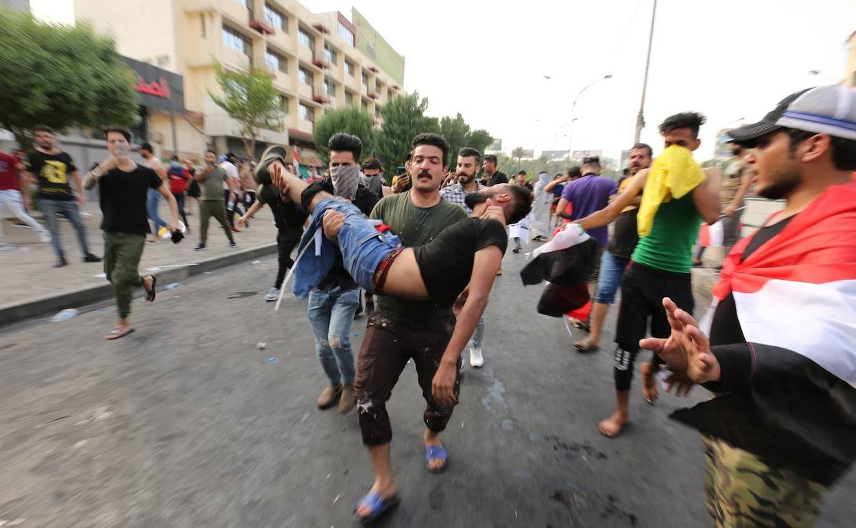 Manifestantee iraquíes llevan a un hombre herido durante un enfrentamiento con las fuerzas antidisturbios.