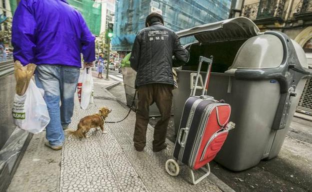 Un hombre busca en el interior de un cubo de la basura en una céntrica calle de Santander.