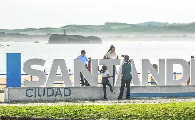 Una mujer saca fotos a los niños, que juegan entre las letras del cartel colocado frente a la playa. 