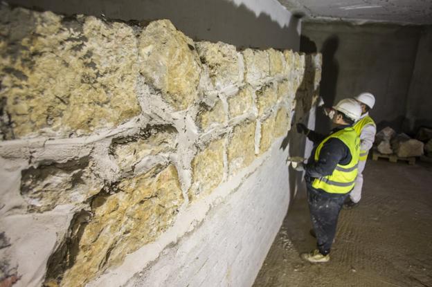 Los operarios trabajan en el muro, recolocando las piedras en su posición original.