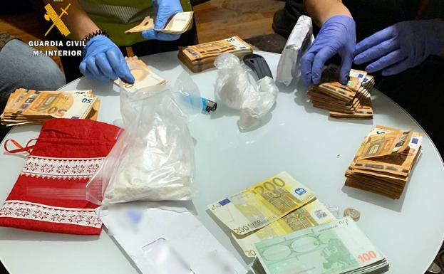 Imagen principal - La Guardia Civil contando el dinero intervenido y muestra de las drogas y utensilios incautados.