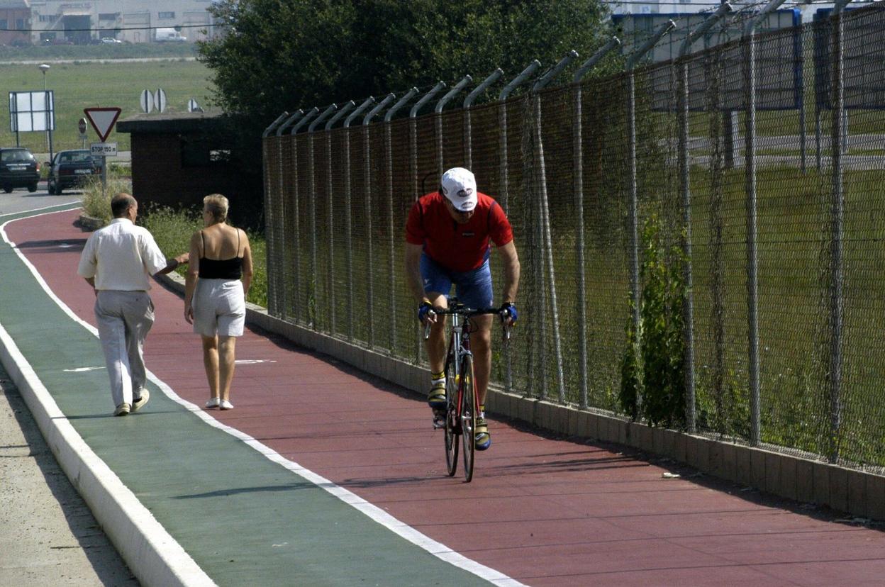 Un ciclista deja atrás a dos paseantes en el carril bici del aeropuerto Seve Ballesteros, en Maliaño (Camargo). 