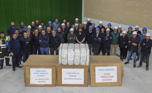 Imagen principal - Arriba, los trabajadores del relevo de tarde posan con la bala de fibra ignífuga. Abajo, Alberto Haya muestra la turbina de uno de los dos generadores de la planta de cogenaración y parte de los 20.000 estéreos de eucaliptos, la madera necesaria para veinticinco días, acumulados en una zona de la fábrica.