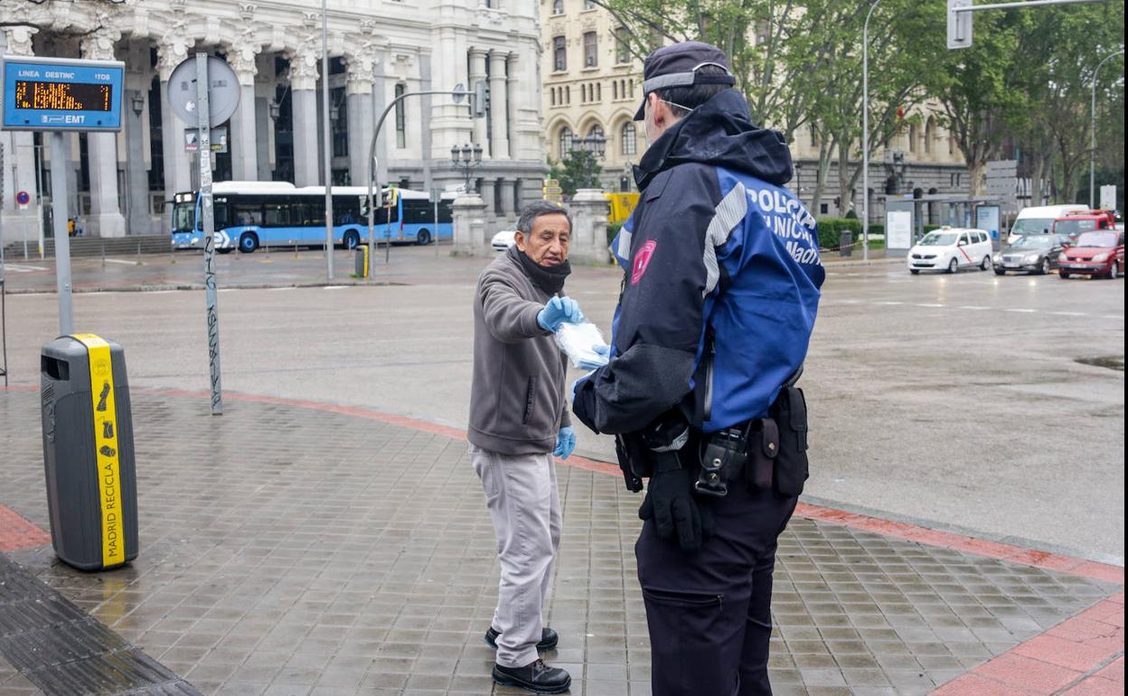 Un agente local de Madrid reparte en la calle mascarillas.