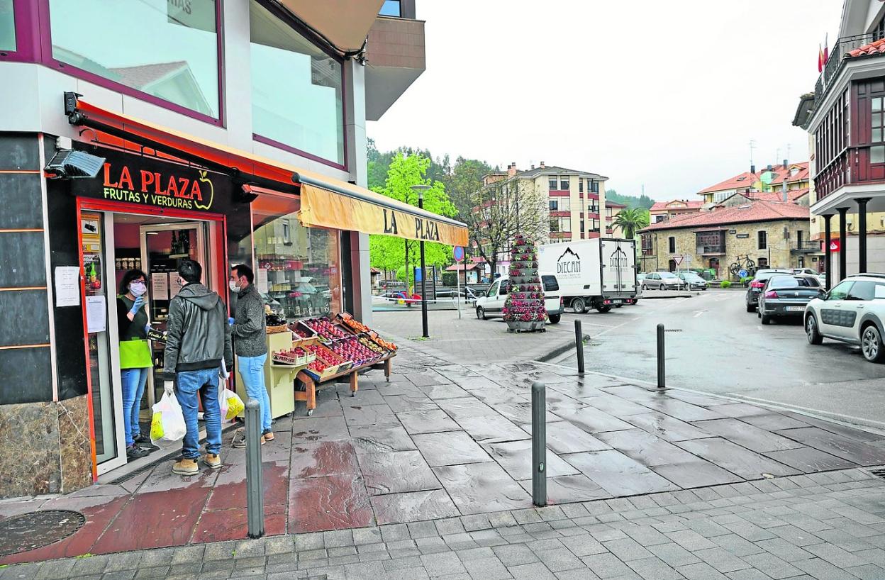 Apertura. Dos clientes esperan fuera de una frutería en el centro de Cabezón de la Sal