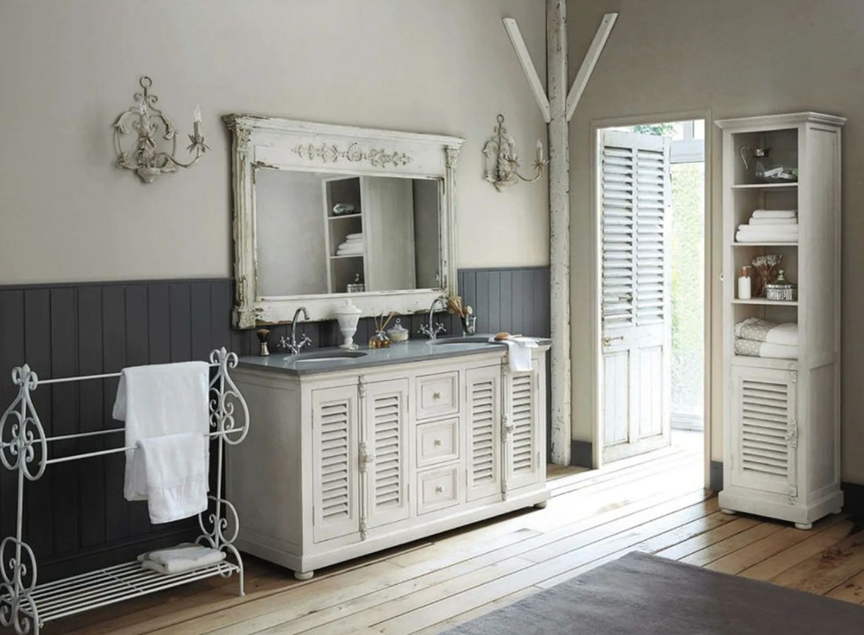 El encanto indudable de piezas como este mueble 'vintage' en blanco roto y gris, creado a través de diferentes materiales, y combinado con un espejo antiguo y una viga de madera al tono, convierte el baño en uno de los rincones más acogedores del hogar.