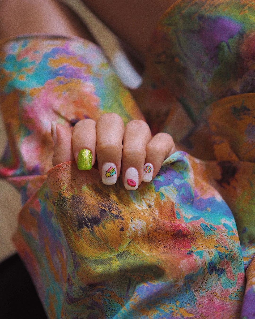 Original manicura de María Fernández-Rubíes con un dibujo infantil diferente para cada uña: un donut, una piruleta, una estrella y un unicornio. Además, en el dedo índice,se completa con un esmalte verde de purpurina. 