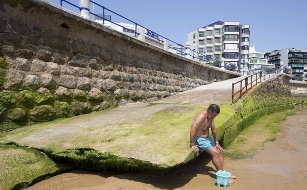 Imagen. Un bañista se sienta en un acceso a la playa cuya rampa no llega a la arena. 