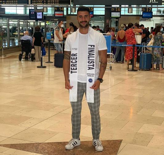 El joven posa en el aeropuerto con la banda oficial del certamen.