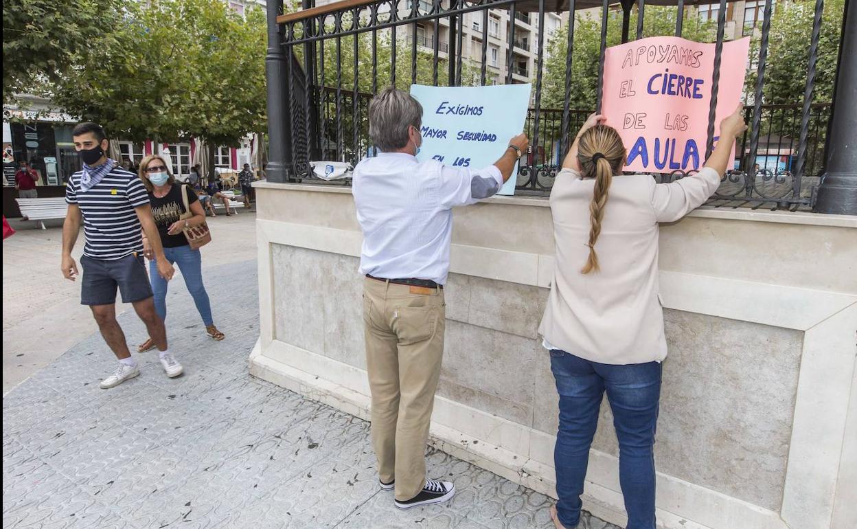 Dos personas colocan carteles en la plaza San Antonio de Santoña pidiendo el cierre de las aulas.