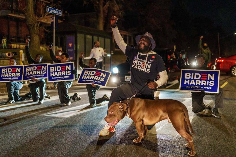 Tyrone Carter, ex jugador de la NFL de Minnesota Vikings, lidera un grupo de niños que apoyan al candidato presidencial Joe Biden, se arrodilla y bloquea la carretera cerca de un lugar de votación en Minneapolis, Minnesota.