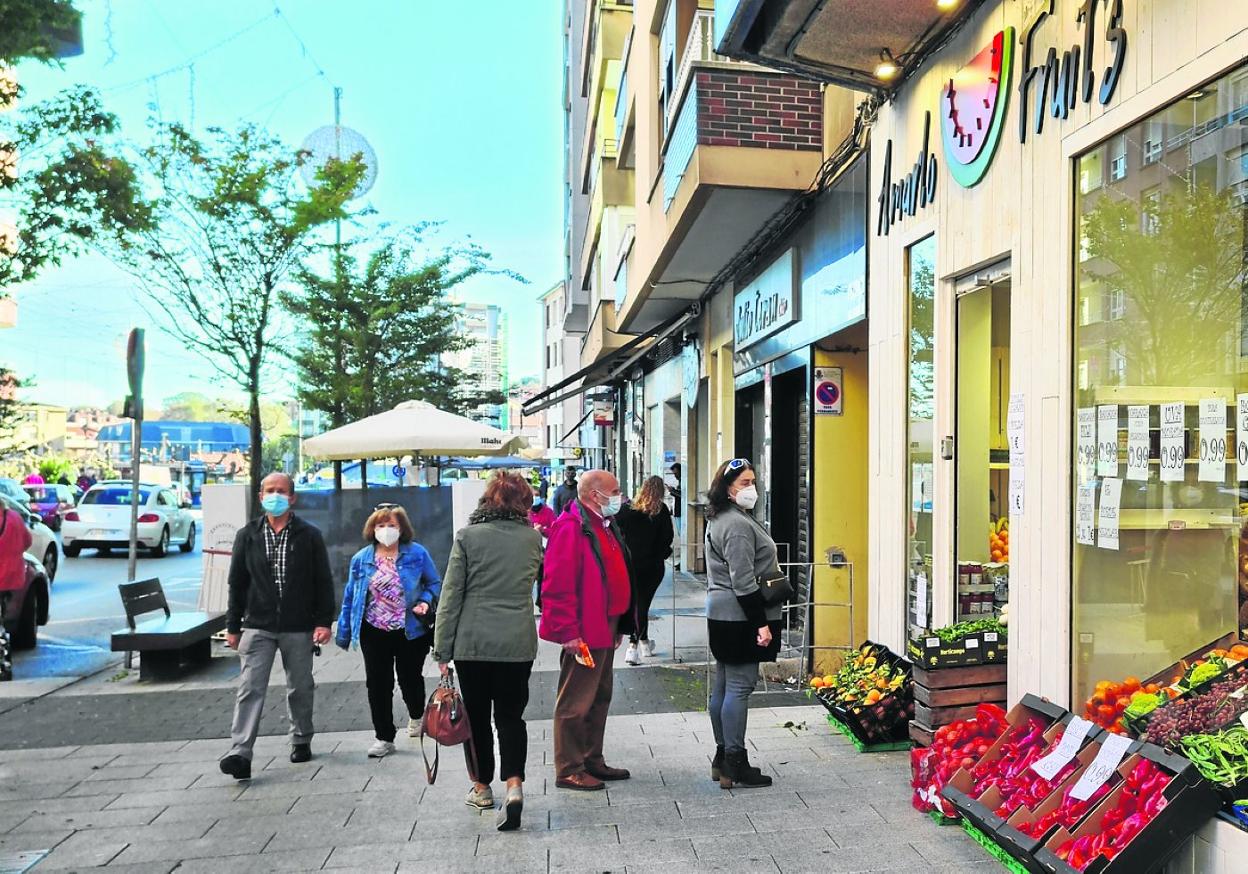 Vecinos y compradores caminan junto a un establecimiento, ayer, en el casco urbano de Maliaño-Muriedas. j. g.