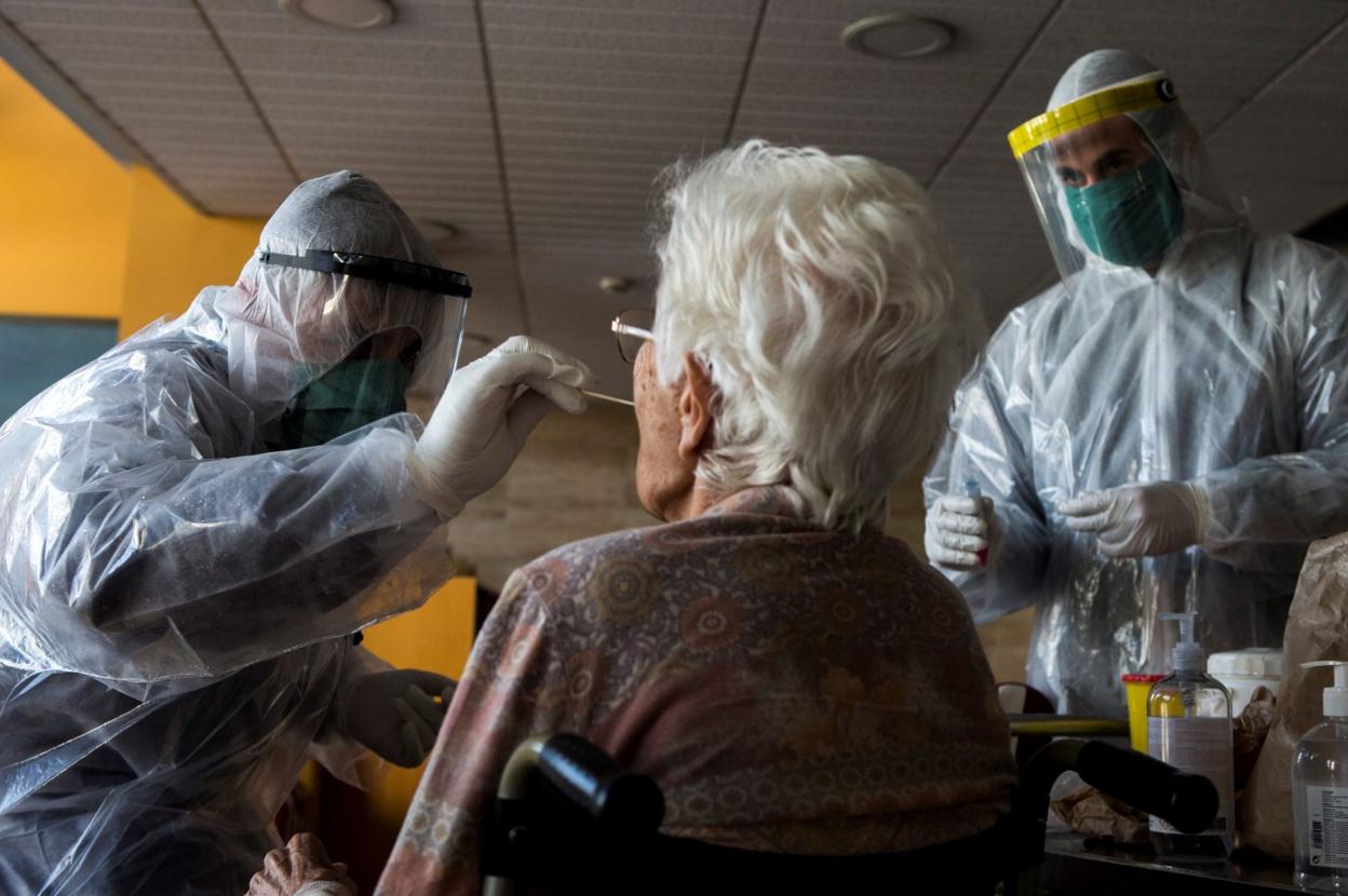 Una pareja de sanitarios toma una muestra a una anciana para practicar una prueba PCR. 