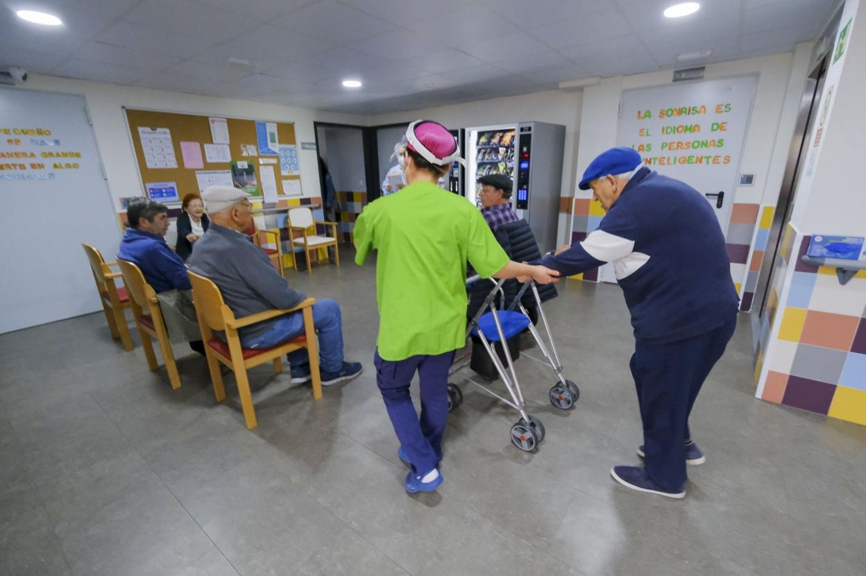 Un trabajador de una residencia ayuda a desplazarse a un usuario. 