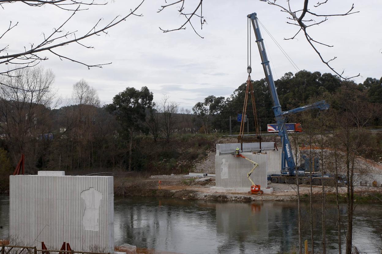 Una grúa coloca la gran viga de hormigón en uno de los lados de la pasarela -el de Ganzo- que irá sobre el río. 