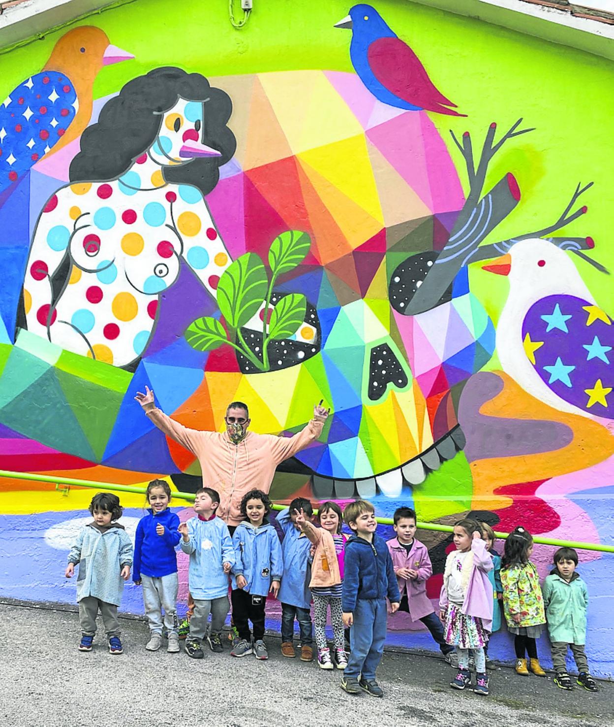 El artista, delante del mural, posa con alumnos del colegio. okuda 