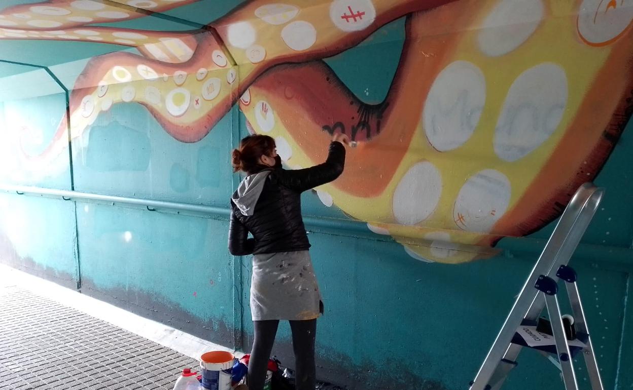 La artista Marina Casaos restaurando uno de sus murales, sobre la vida submarina, que ha sido dañado con grafitis.