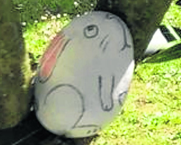 Una roca con el dibujo de un conejo escondida sobre el tronco de un árbol