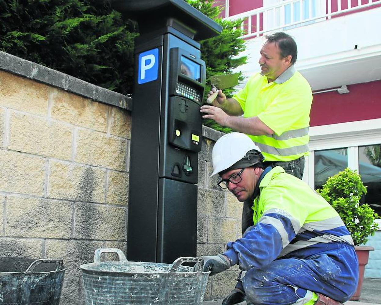 Dos operarios, este viernes, terminando de instalar un parquímetro en Somo. 