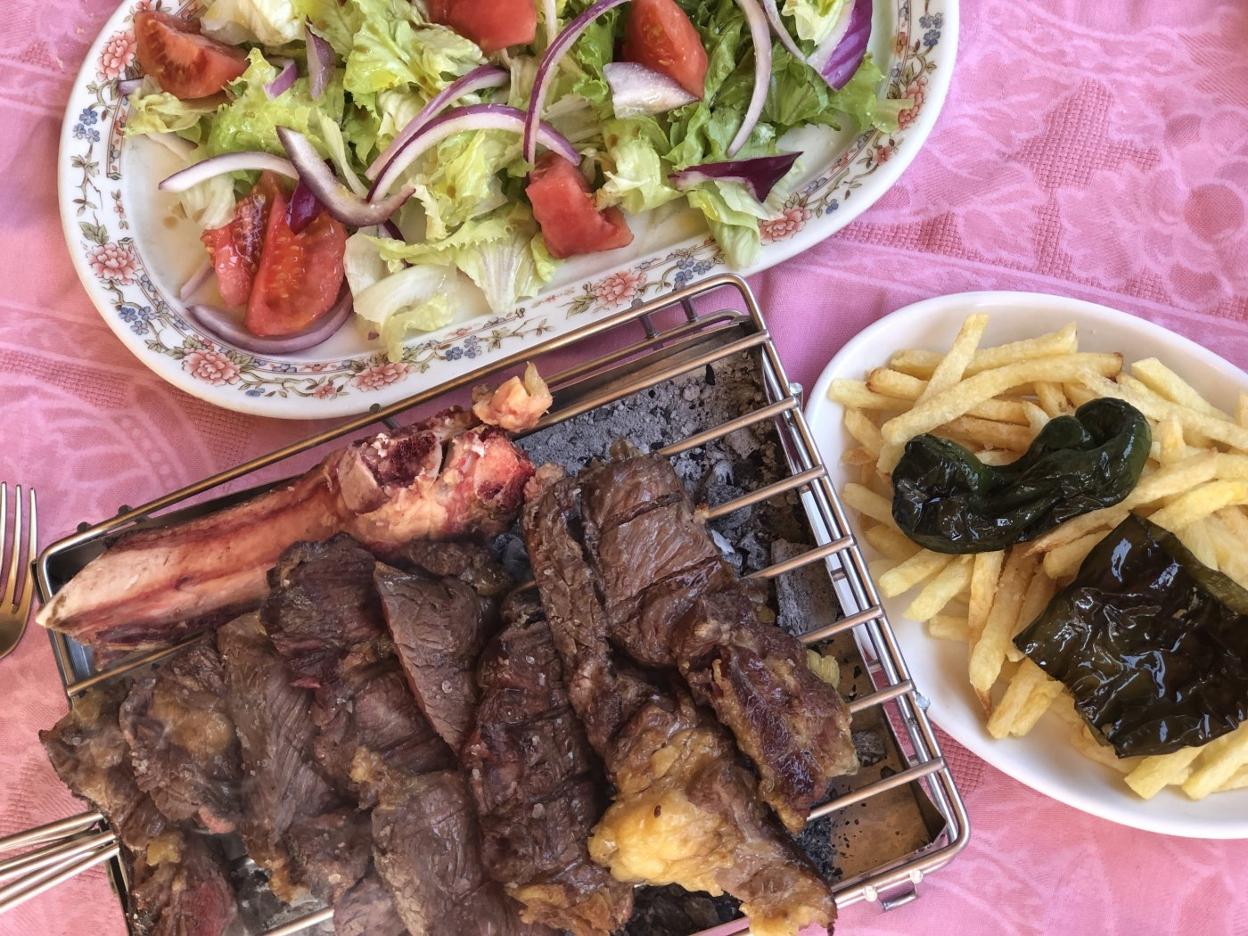 Chuletón de un kilo sobre parrilla, ensalada y patatas fritas. 