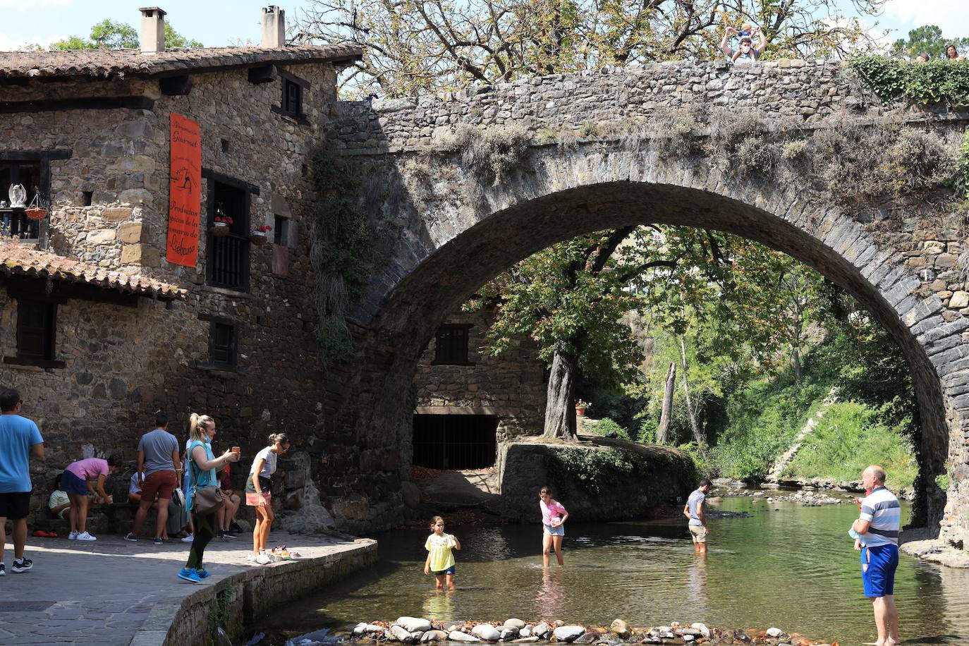 Un grupo de turistas se refresca en el río Quiviesa, junto al puente medieval de San Cayetano, en Potes