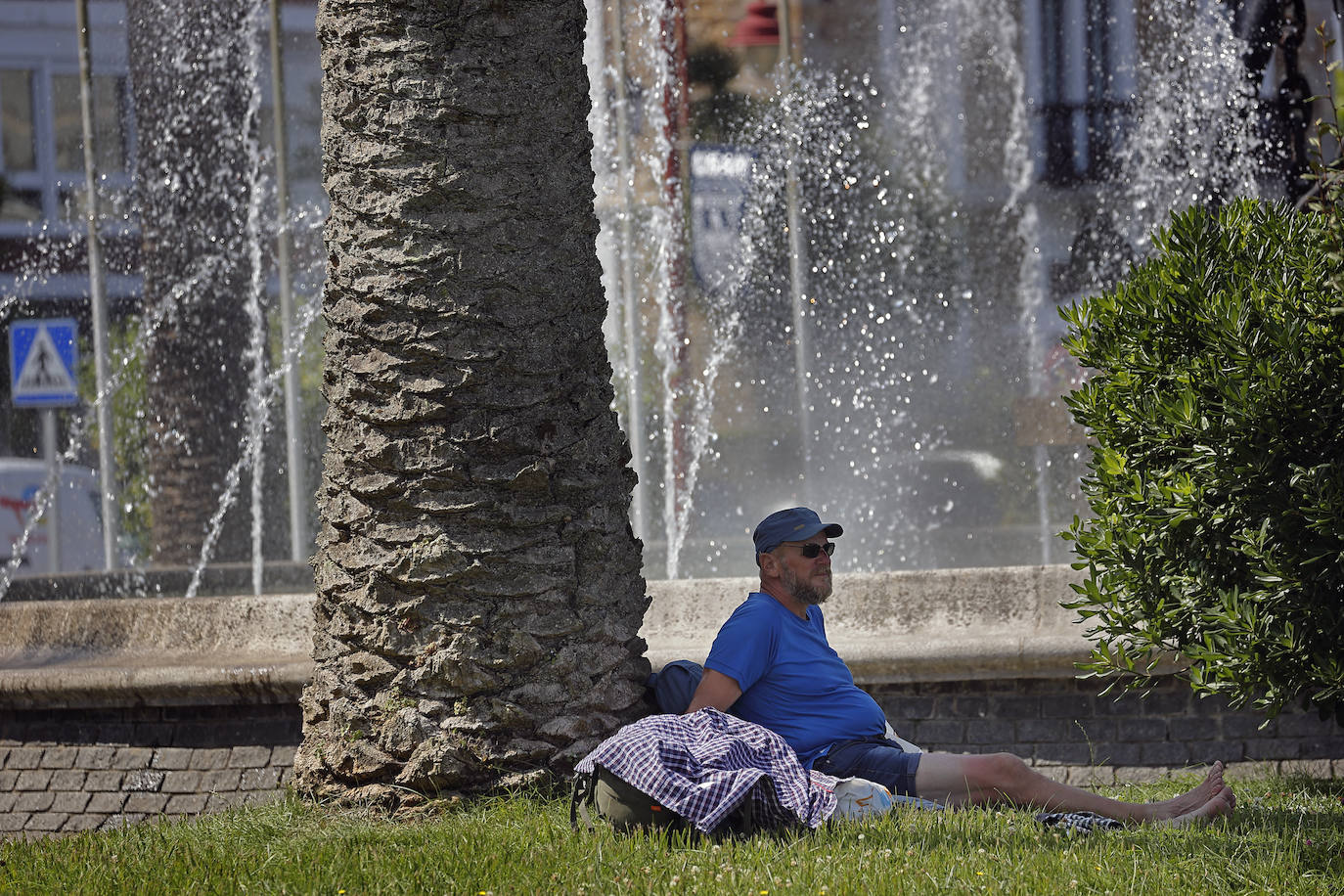 Un hombre descansa a la sombra un parque de San Vicente de la Barquera