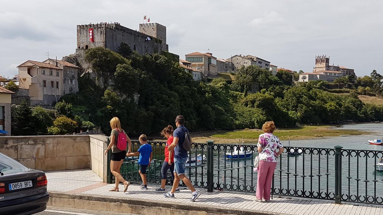 Un grupo de turistas pasea por el Puente de la Barquera, con el Castillo del Rey y la iglesia de Santa María de los Ángeles al fondo. 