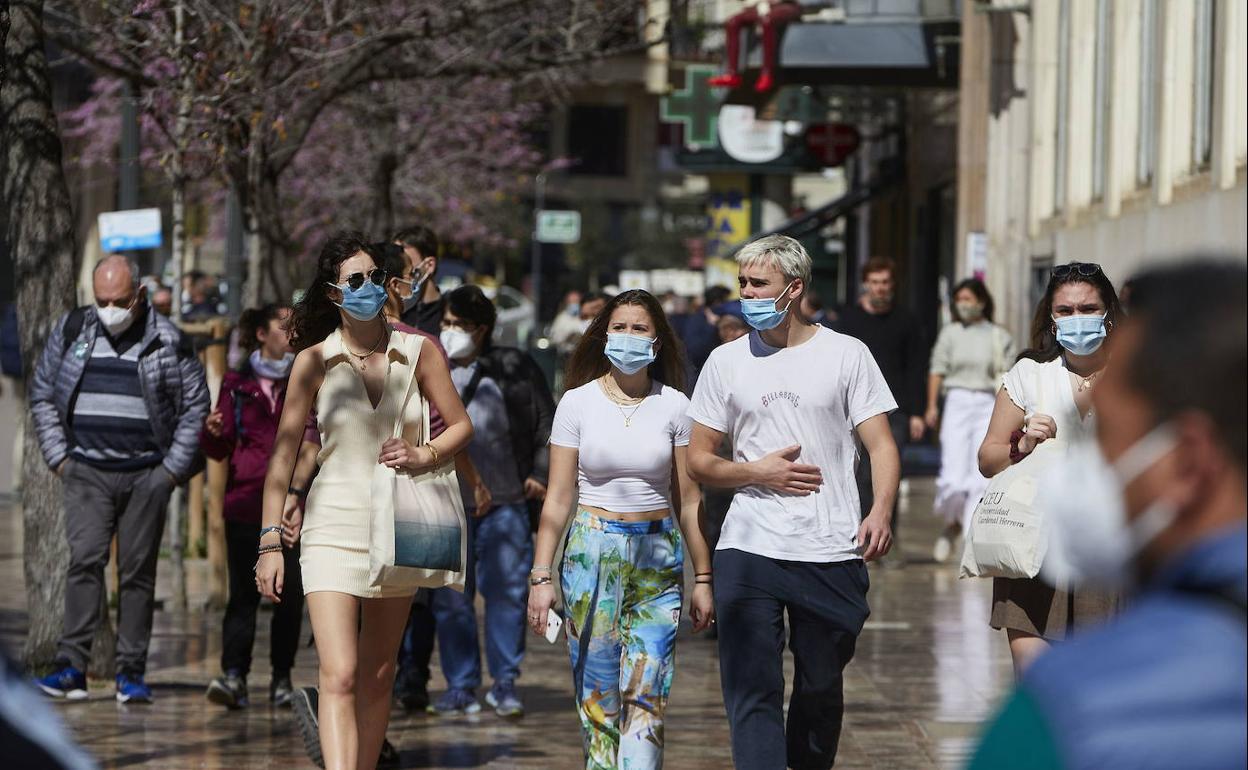 Perdsonas pasean por una calle de Valencia portando mascarillas. 