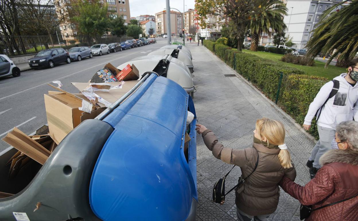 Dos vecinas hacen uso de un contenedor de basura roto y lleno en la calle General Dávila. 