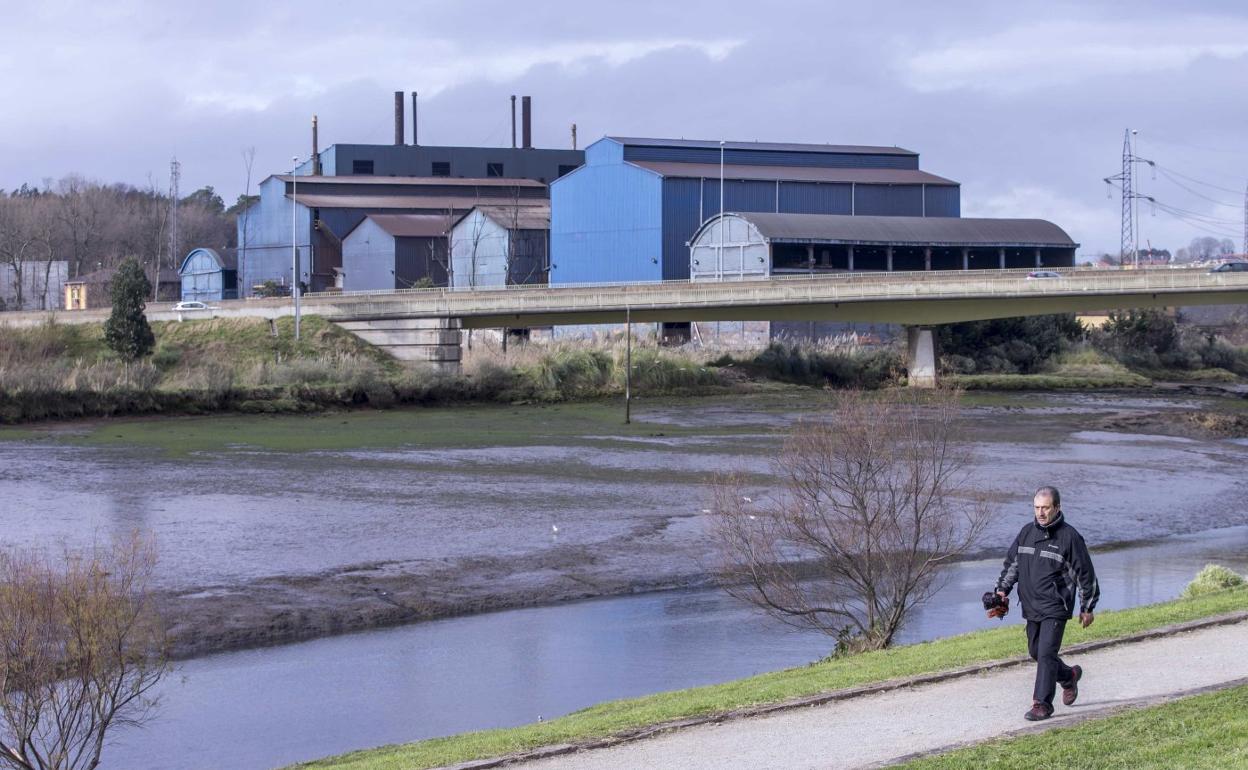 Un vecino pasea junto a la ría del Carmen, con Ferroatlántica al fondo, entre Camargo y El Astillero. 