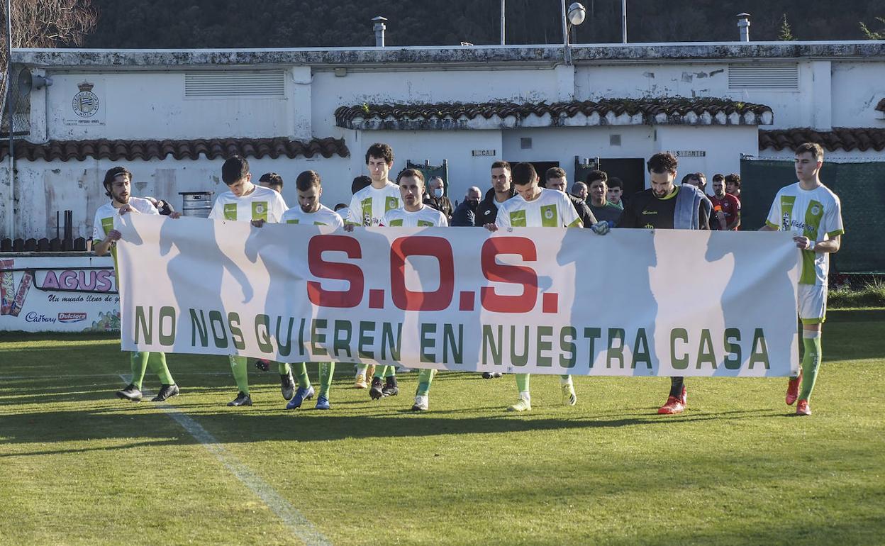 Los jugadores del Noja saltan al campo de La Caseta con la pancarta para protestar por la situación del club. 