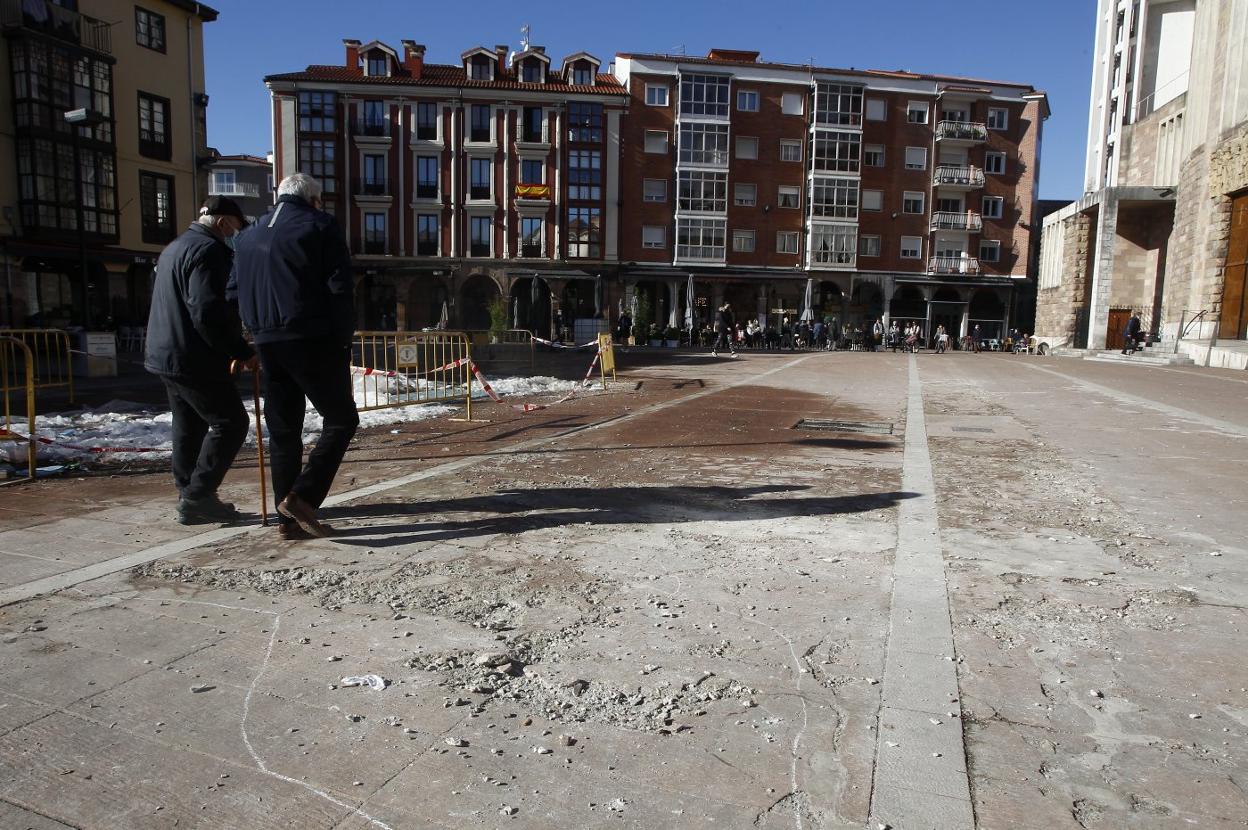 Dos vecinos caminan junto a los daños provocados en el pavimento de la plaza por la pista de hielo. 